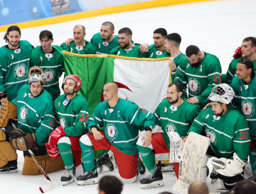 A photo of the Algeria national ice hockey team wearing green uniforms holding a large Algeria flag